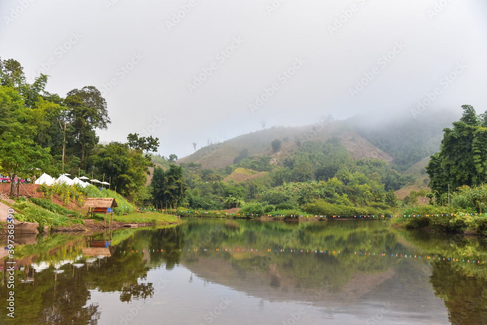 The view of the natural stream on the mountain is covered with mist. There are tourist tents by the stream as well.