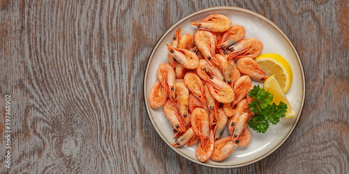 Boiled shrimp prawns in a shell with lemon and parsley in a plate on a wooden background. Top view