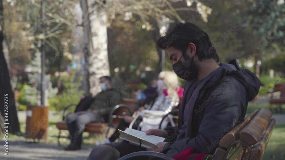 Covid19 Mask. Man drinking coffee while reading a book in the park. Covid19 Mask. Man drinking coffee while reading a book in the park.