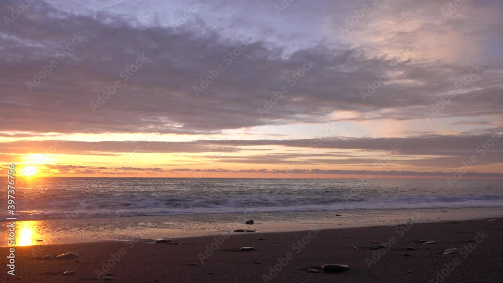 Evening. The sun is low on the horizon. There are beautiful clouds in the sky, highlighted in pink and orange. Sea waves roll onto the beach and foam. Sunny path on the water and on the sand Evening. The sun is low on the horizon. There are beautiful clouds in the sky, highlighted in pink and orange. Sea waves roll onto the beach and foam. Sunny path on the water and on the sand