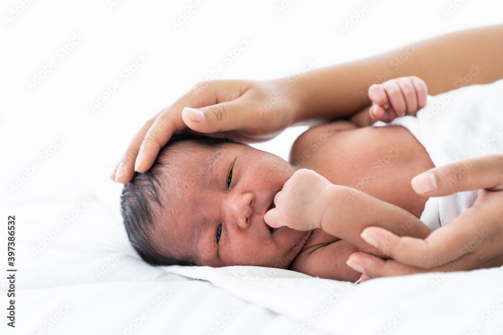 African American newborn baby or infant lying on white bed while mother’s hands takes care and comforting. Family, love and new life concept African American newborn baby or infant lying on white bed while mother’s hands takes care and comforting. Family, love and new life concept