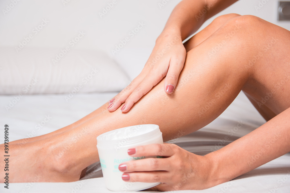 woman putting hand cream on her legs to keep them hydrated and healthy. Wellness, health and lifestyle concept woman putting hand cream on her legs to keep them hydrated and healthy. Wellness, health and lifestyle concept