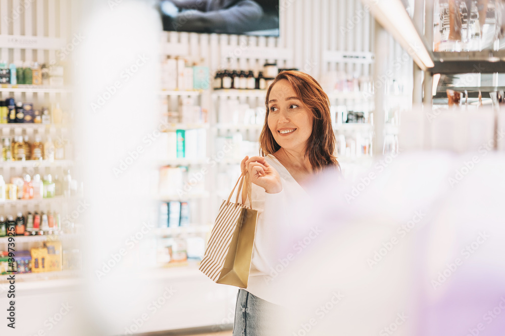 Adult pretty smiling woman with dark hair in the cosmetics and perfume store, holiday shopping Adult pretty smiling woman with dark hair in the cosmetics and perfume store, holiday shopping