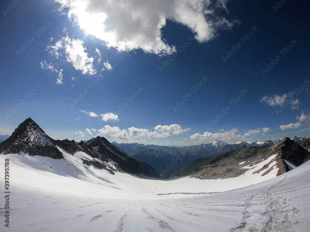A footprints on the snow, lying on a glacier under Hohe Sonnblick in Austrian Alps. The footprints lead in one direction. Many high mountain chains in the nearby. Clear and sunny day. Mountainerring