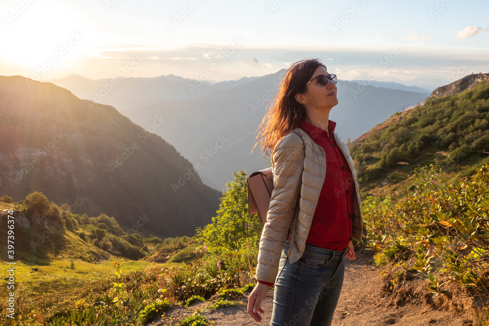 Happy young woman in the mountains. Tourist in a backpack in the mountains walking in the Alpine meadows.