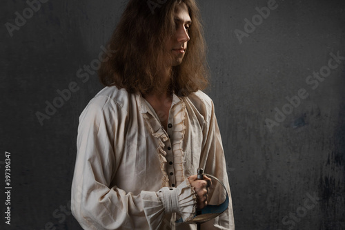 Romantic young man in a medieval costume with a sword in his hands, a musketeer in a fighting stance, photo