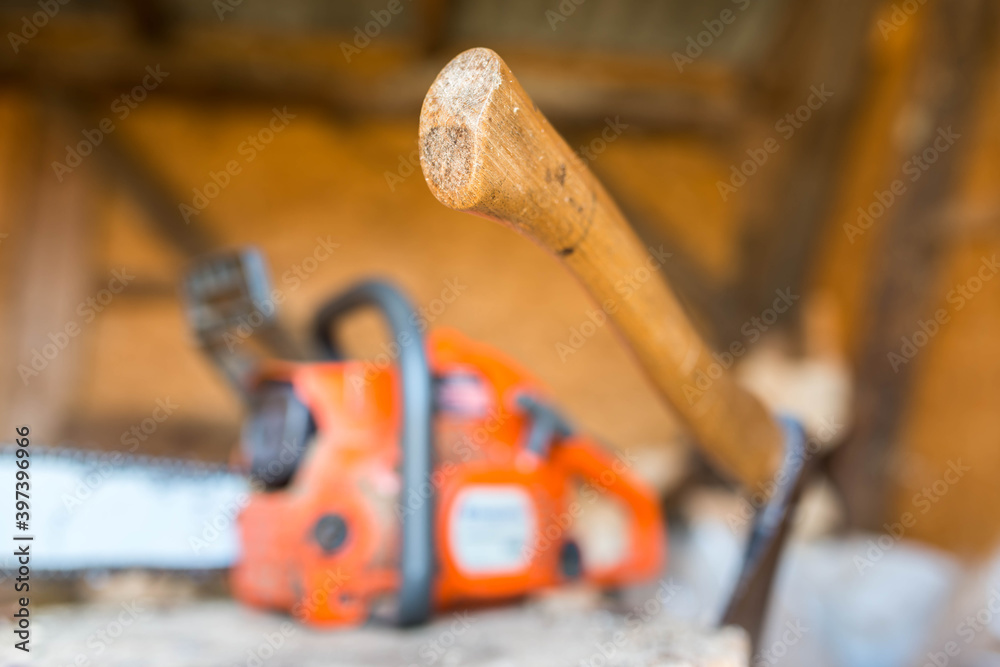 Chainsaw, axe with wood handle on beech wood log, focus on the handle, shallow depth of field.