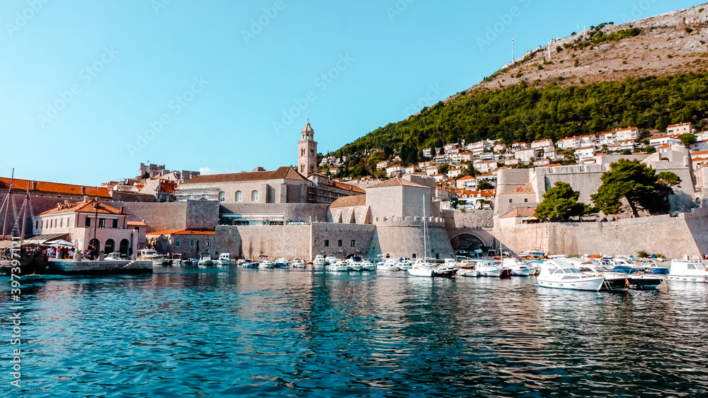View of Dubrovnik from Old City Port. View of Dubrovnik ciry walls, red rooftops, and a tower with boats docked in old city harbor