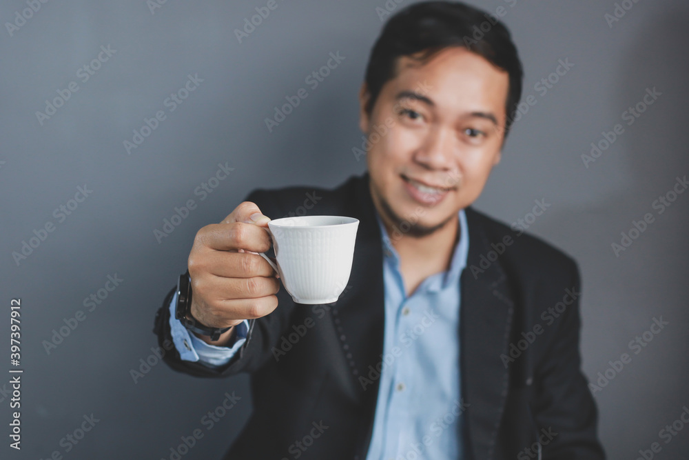 Hand of businessman holding a cup of coffee with blurry of businessman on the grey background. Selective focus on cup Hand of businessman holding a cup of coffee with blurry of businessman on the grey background. Selective focus on cup