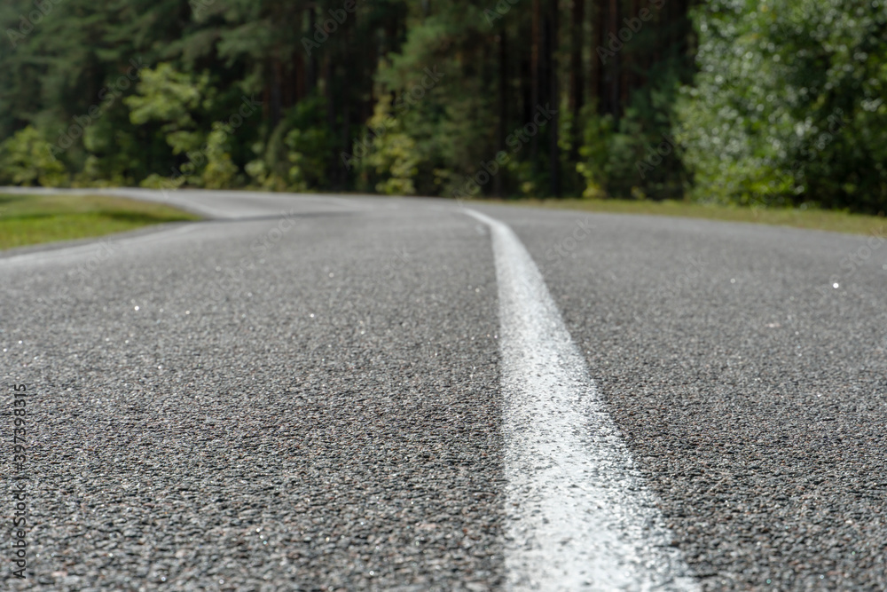 Empty asphalt road through woods and fields. New fresh asphalt pavement away from the city. Development of rural infrastructure. Road marking lines close up. Empty asphalt road through woods and fields. New fresh asphalt pavement away from the city. Development of rural infrastructure. Road marking lines close up.