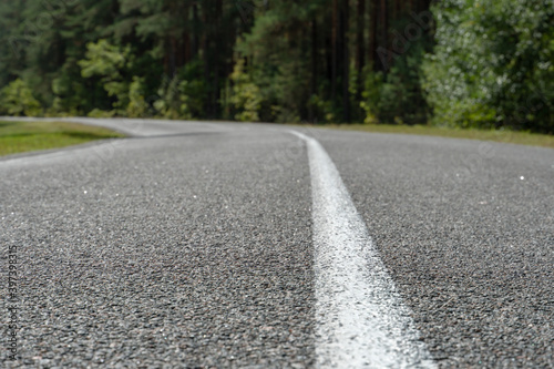 Empty asphalt road through woods and fields. New fresh asphalt pavement away from the city. Development of rural infrastructure. Road marking lines close up.