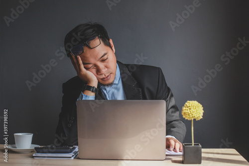 Businessman falling asleep at office desk with closed eyes, overworked young man, unmotivated worker sleeping at workplace, boring routine work photo