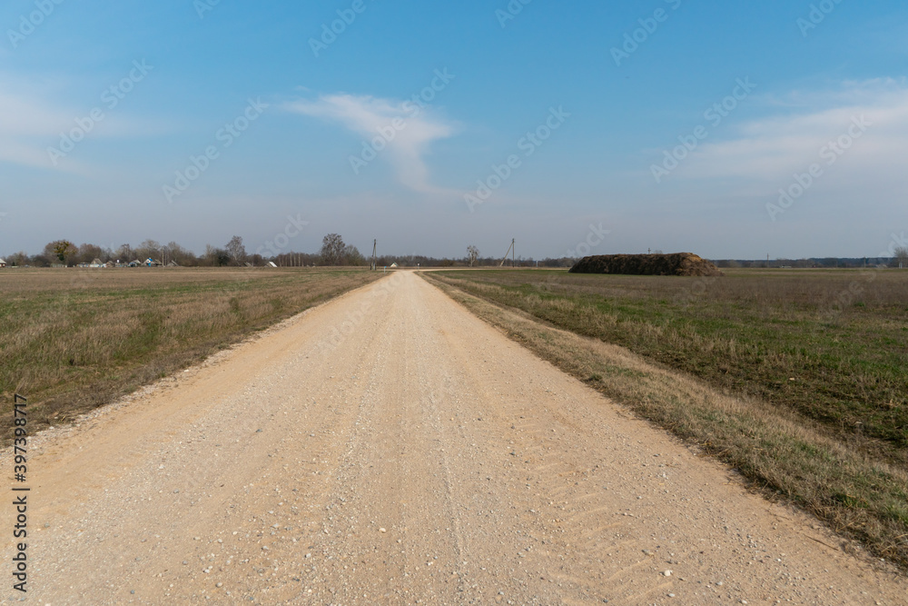 Naklejka premium Empty dirt road through the fields. Fluffy clouds on a warm summer Sunny day over a field of wheat. Pure nature away from the big city. Eco tourism.