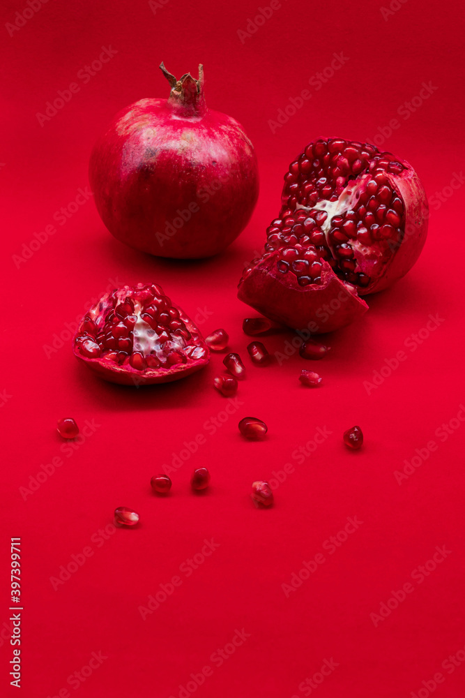 Fotografie Unbroken and broken pomegranates on red background