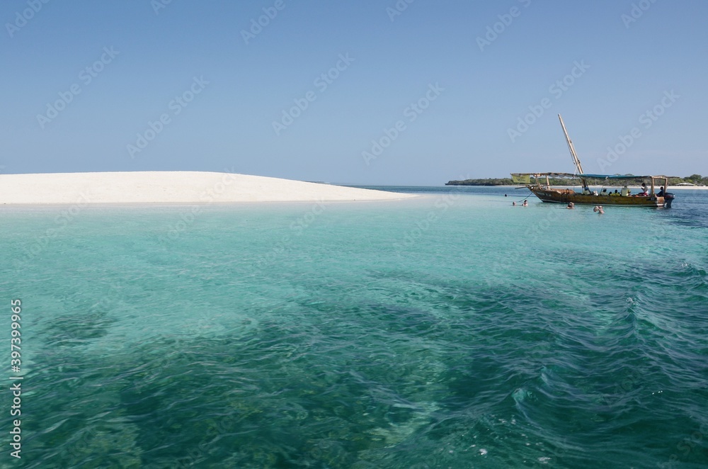Sandy island off the coast of Zanzibar, Tanzania. Blue sky, white sand, crystal clear water, sailboat, Indian ocean