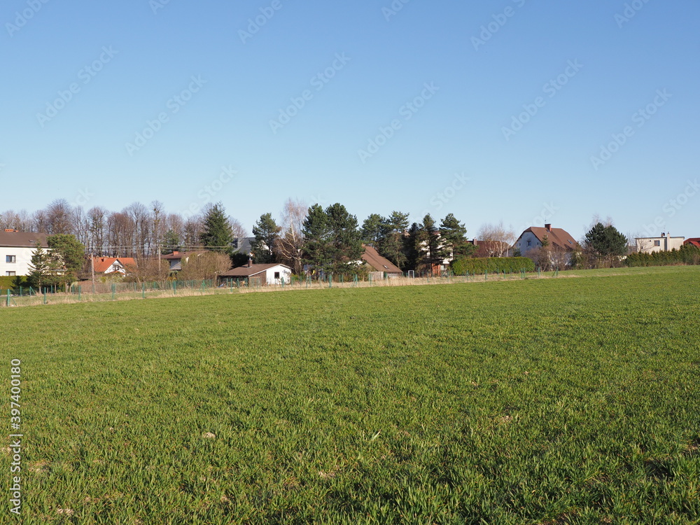Green field and houses at european Bielsko-Biala city in Silesian district in Poland, clear blue sky in 2020 warm sunny spring day on April. Green field and houses at european Bielsko-Biala city in Silesian district in Poland, clear blue sky in 2020 warm sunny spring day on April.