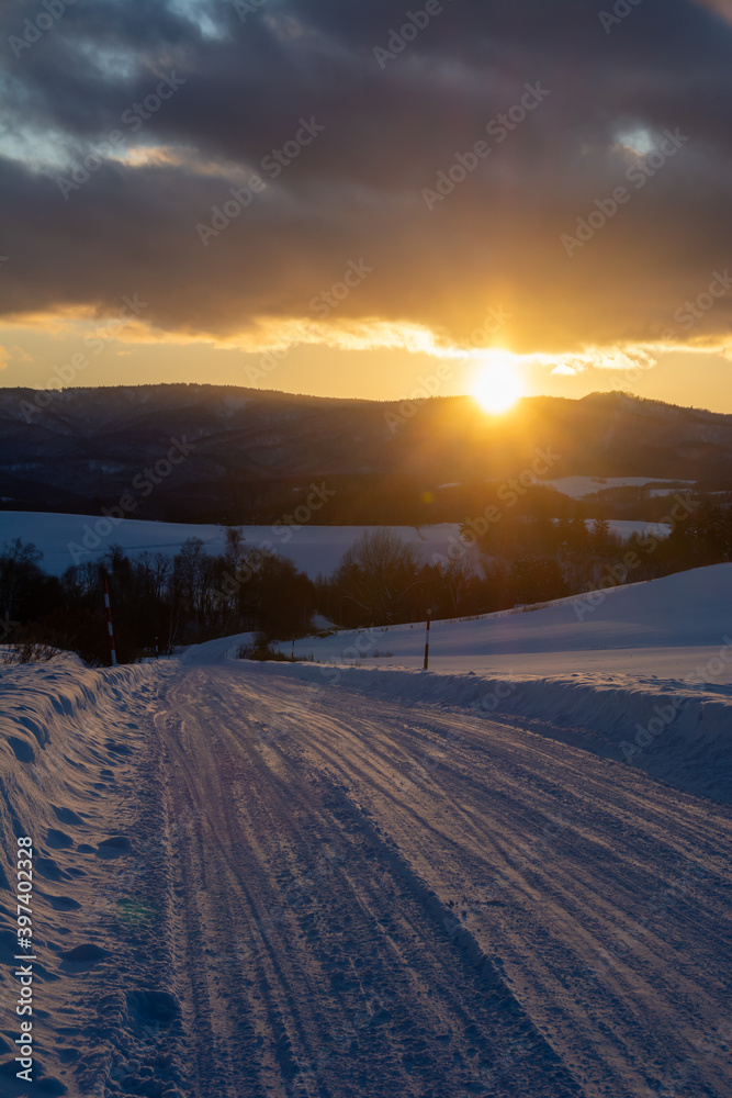 冬の夕暮れの道路と山陰に沈む太陽
