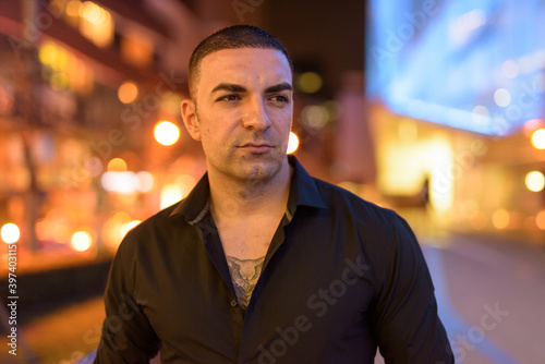 Portrait of handsome man with short hair thinking outdoors at night in city