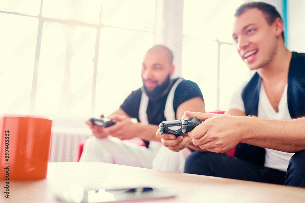 Friends and video games. Two handsome young men playing video games while sitting on sofa Friends and video games. Two handsome young men playing video games while sitting on sofa