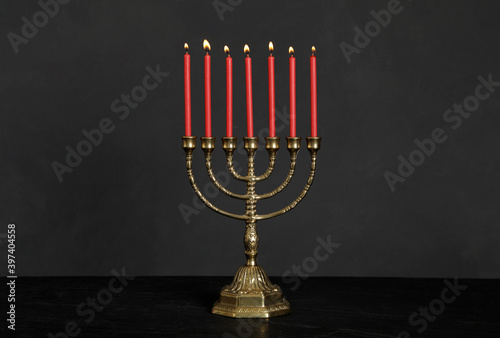 Golden menorah with burning candles on table against black background