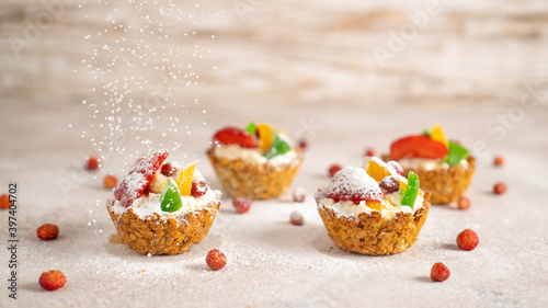 Sprinkling icing sugar over healthy cupcakes with cottage cheese, strawberries, banana, dried fruits. New Year background