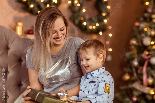 Smiling young girl and boy sit in a decorated Christmas room and enjoy the holiday and gifts.