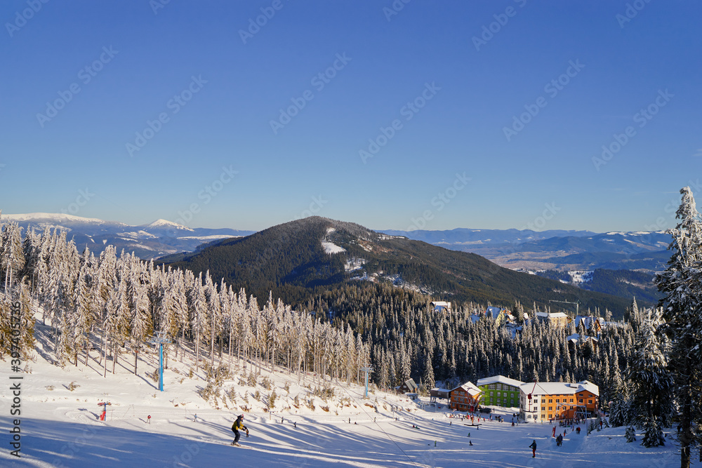 Snowy mountains and ski lifts. Skiers and snowboarders skiing downhill to village.