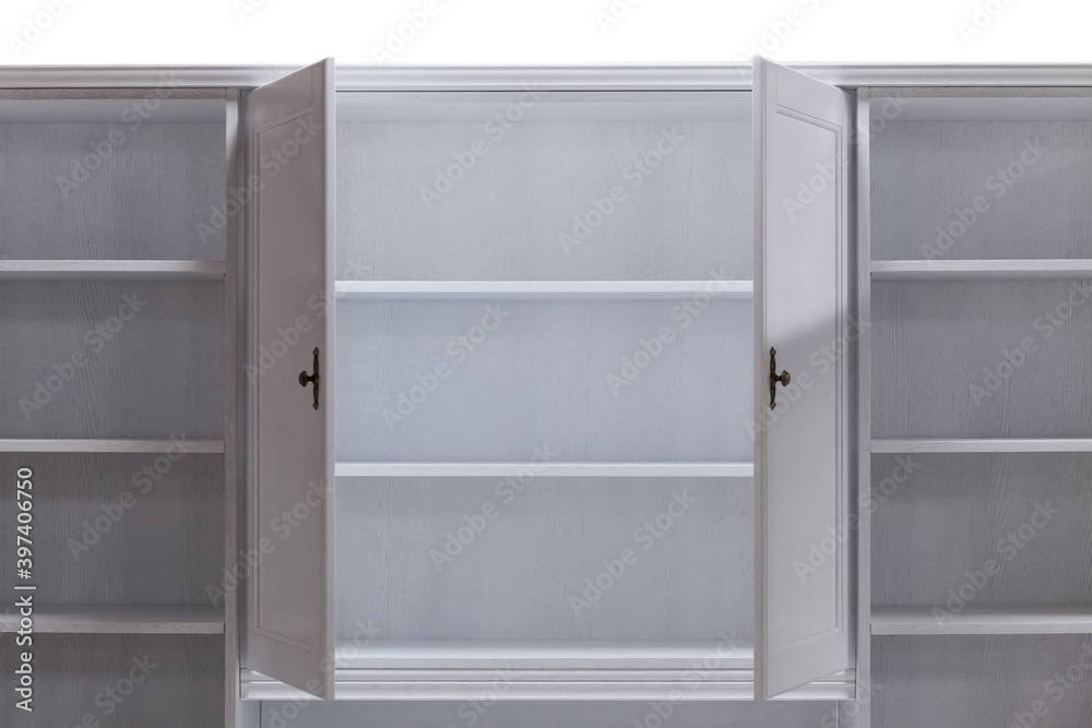 Open doors of a white wooden kitchen cabinet with shelves. Classical furniture made of natural wood.