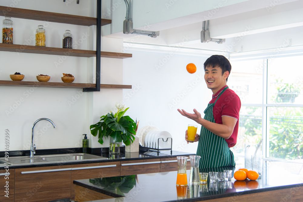 Portrait smart and handsome Asian man preparing healthy meal and drinking fresh organic orange juice in the loft style kitchen.