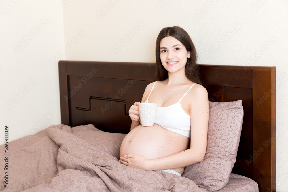 pregnant young woman sitting on bed and drinking coffee at home. maternity concept pregnant young woman sitting on bed and drinking coffee at home. maternity concept
