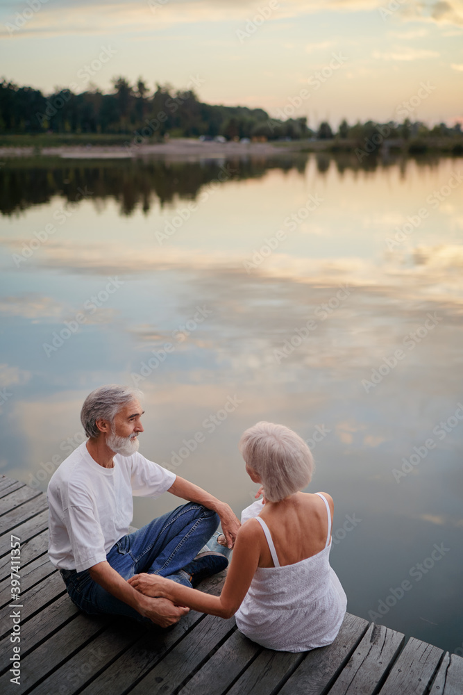 Romantic holiday. Senior loving couple sitting together on lake bank. Romantic holiday. Senior loving couple sitting together on lake bank.