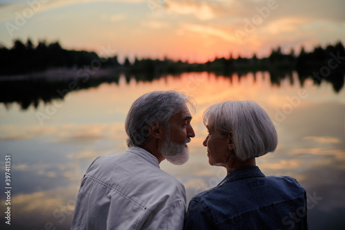 Romantic holiday. Senior loving couple sitting together on lake bank enjoying beautiful sunset. © luengo_ua