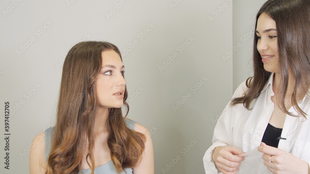 Master beautician communicates with the client before the procedure. Young woman in a white robe smiles affably at her beautiful client. Female doctor tells the features of the procedure to patient Master beautician communicates with the client before the procedure. Young woman in a white robe smiles affably at her beautiful client. Female doctor tells the features of the procedure to patient