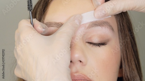 Cosmetologist's hands stick the strip to the eyebrow to remove warm wax excess hair from the eyebrow with a special strip. Wax correction of the shape of the eyebrows. Beauty industry close up.