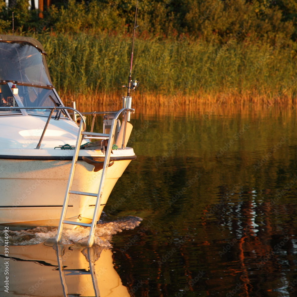 White plastic cabin motor boat bow deck with railing with stairs floating  on river calm water on green grass shore background at Sunny summer  evening, outdoor holidays recreation Stock Photo