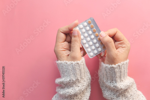 women hand holding birth control pills on pink background 