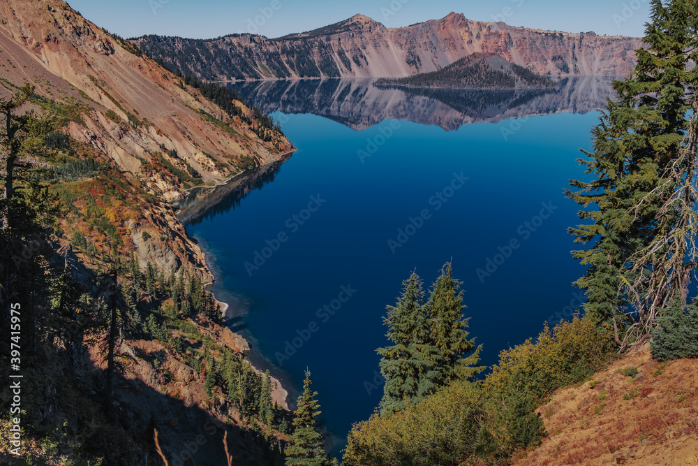 Pine trees, Deep blue lake reflections and Wizard Island at Crater Lake National Park, Oregon, USA. 