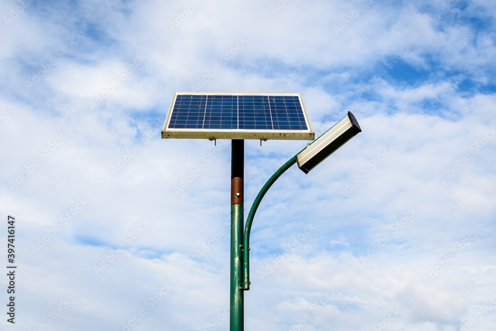 Lighting pole activated with an attached blue solar panel in Parcul Izvor (Izvor Park) in Bucharest, Romania, with cloudy sky in the background, in a summer day. Lighting pole activated with an attached blue solar panel in Parcul Izvor (Izvor Park) in Bucharest, Romania, with cloudy sky in the background, in a summer day.