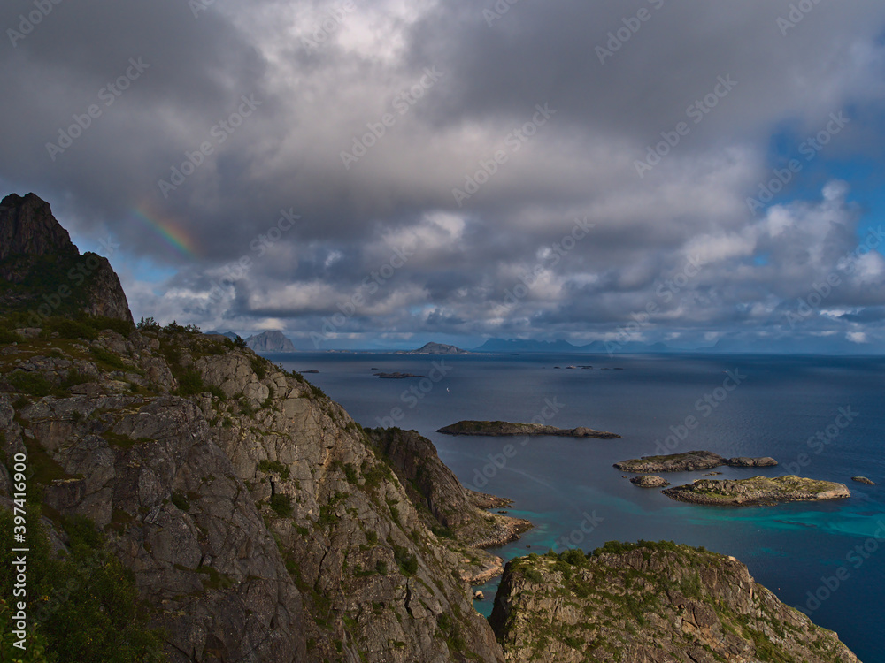 Beautiful aerial panoramic view of coast of Norwegian Sea on Austvågøya island near Henningsvær, Lofoten, Norway with rugged mountains and light rainbow on sunny day in late summer with cloudy sky.