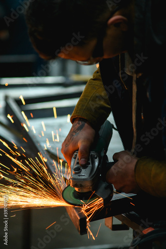Metal worker in safety googles polishing metallic profile with angle grinder in workshop 
