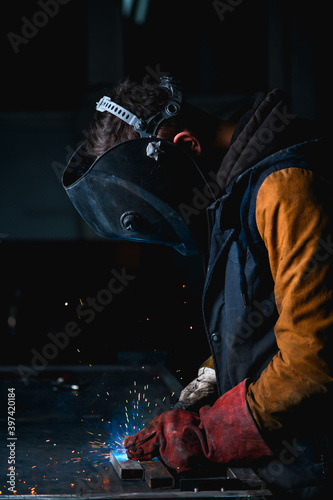 Welder in mask with visor working in metal on workbanch in factory 