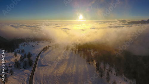 Aerial drone flight between clouds during winter season. A pale sun shines above the clouds after a cold and snowy blizzard.