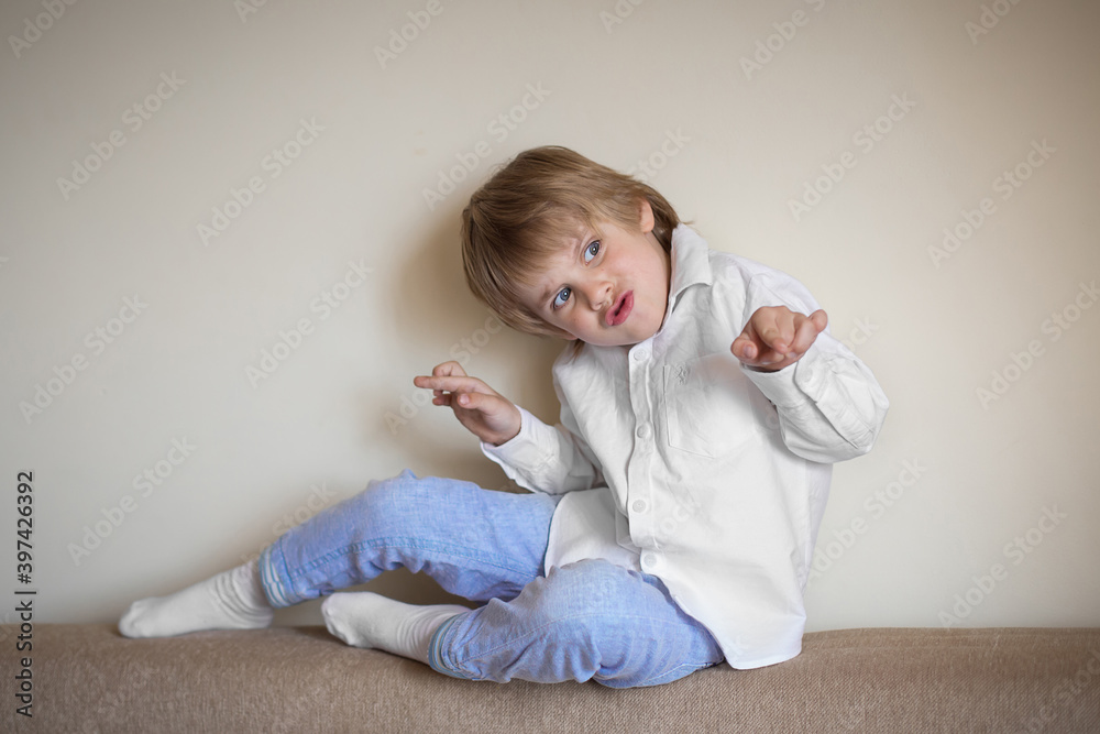 A five-year-old boy in a white shirt and blue pants is sitting in a beige room A five-year-old boy in a white shirt and blue pants is sitting in a beige room