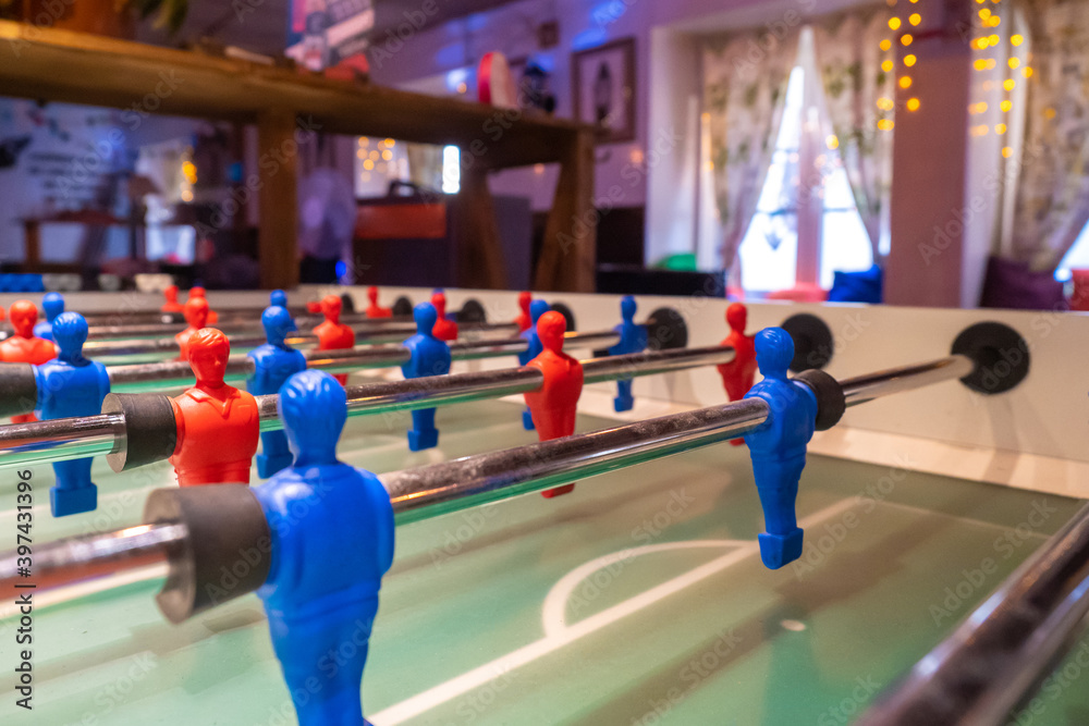 Fototapeta The game of table football. Table football field on the background of the recreation room. Games for children and adults. Enthusiasm. Battle. Desire to win. We help plastic players score goals.