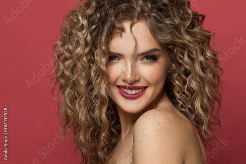 Pretty model woman with curly hair smiling on red background