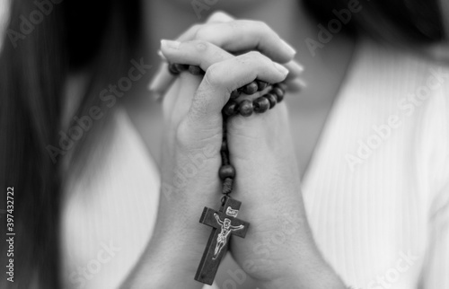 Niña cristiana rezando con un rosario en las manos, en blanco y negro.