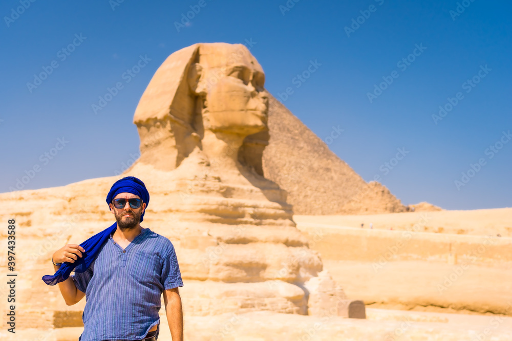 A young tourist at the Great Sphinx of Giza dressed in blue and a blue turban, from where the miramides of Giza. Cairo, Egypt