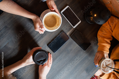 Top view of female hands with smartphones and cups of coffee on a table in a cafe. Three girlfriends drinking coffee.