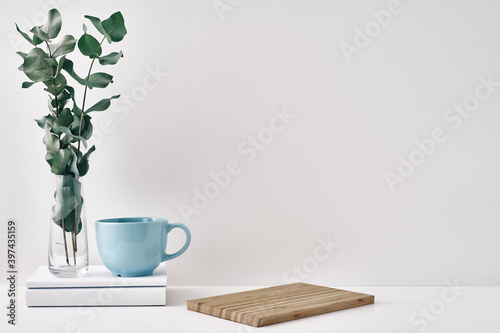 A mug  a stack of books  a wooden board and a transparent vase with eucalyptus branches. Eco-friendly materials in interior decor  minimalism. Copy space  mock up