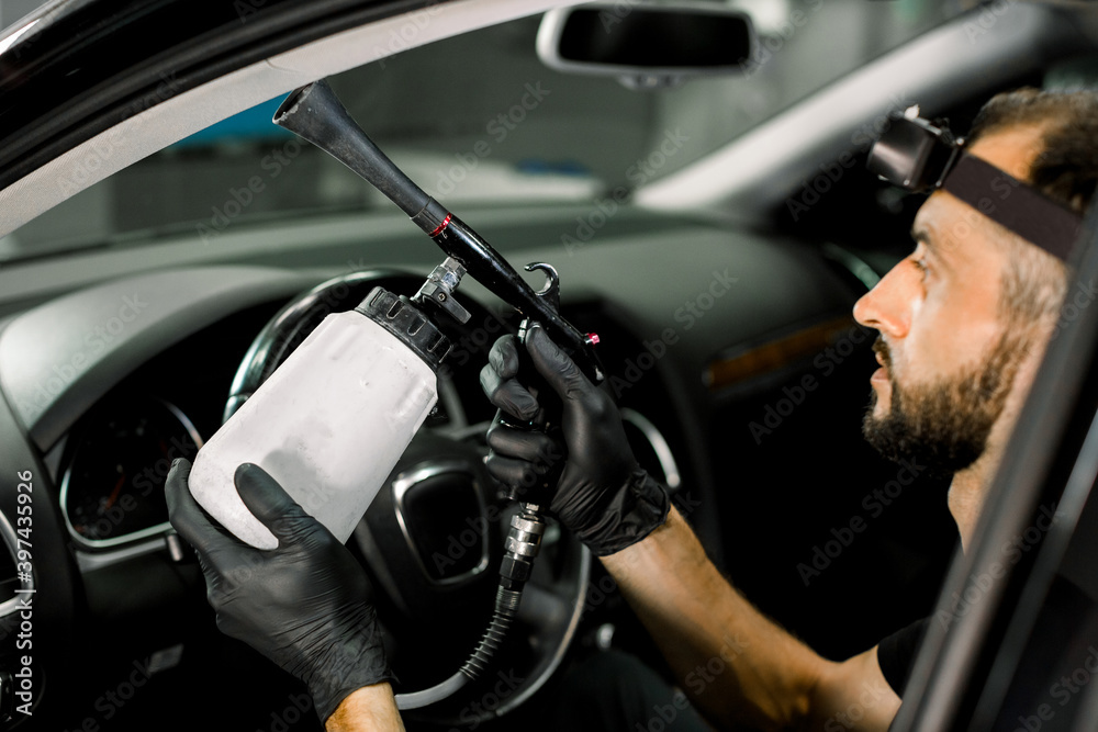 Car wash service. Male worker cleaning automobile salon with air gun, closeup. Professional chemical cleaning of vehicle interior with aero gun machine